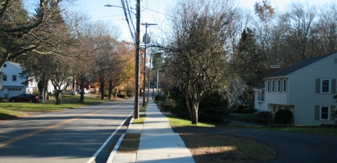 This figure is an image showing a pedestrian path used by students to reach their school bus pickup point. There is a basketball hoop at the end of the nearby street.